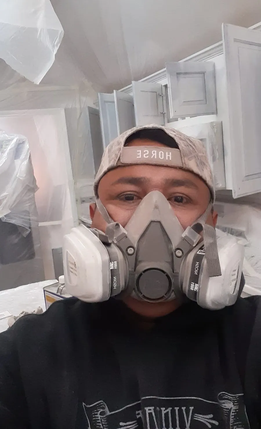 Painter in a respirator spraying kitchen cabinets with the room fully covered