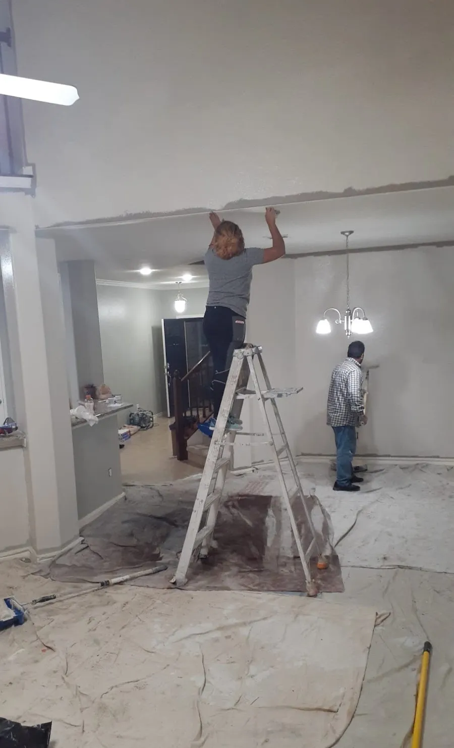 Painters working on a ceiling and walls in a covered living room